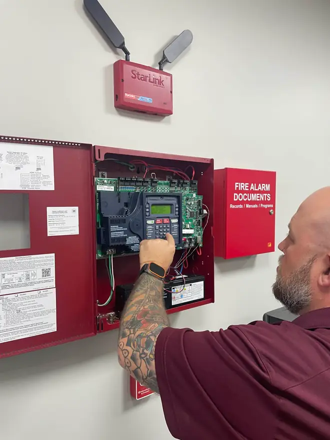 Technician working inside an open fire alarm control panel below a StarLink communicator