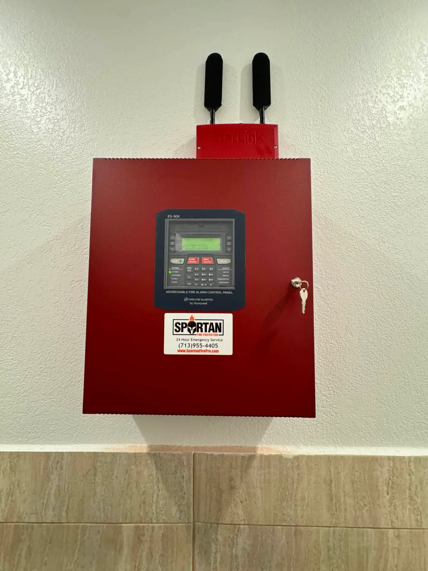 Red fire alarm control panel with a Spartan service sticker and a StarLink communicator