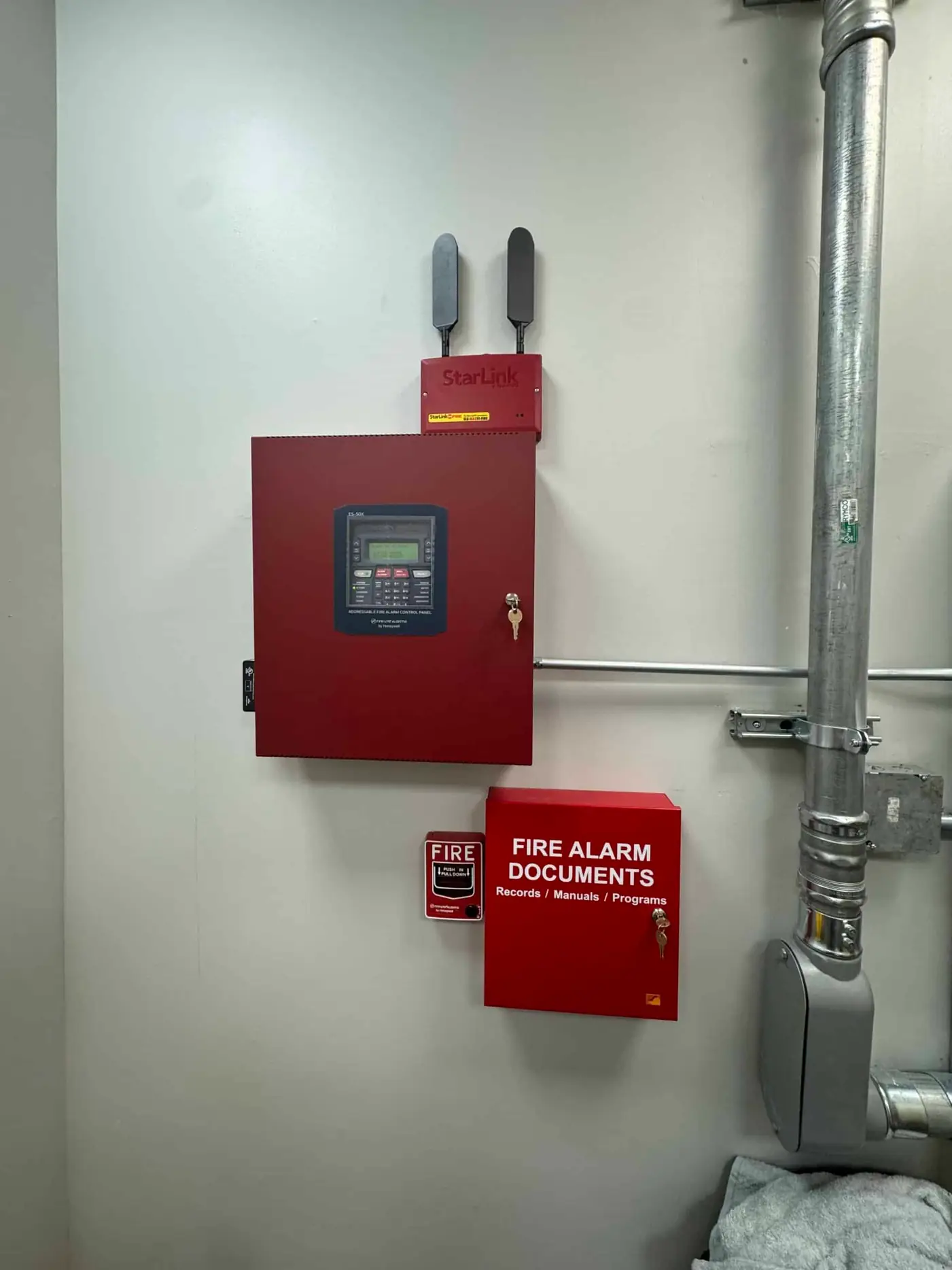 Fire alarm control panel and documents box mounted beside a steel pipe