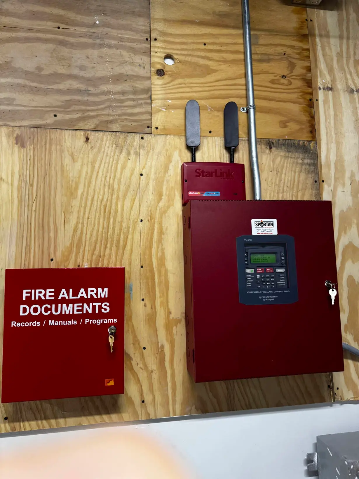 Newly installed fire alarm control panel and documents box on a plywood wall