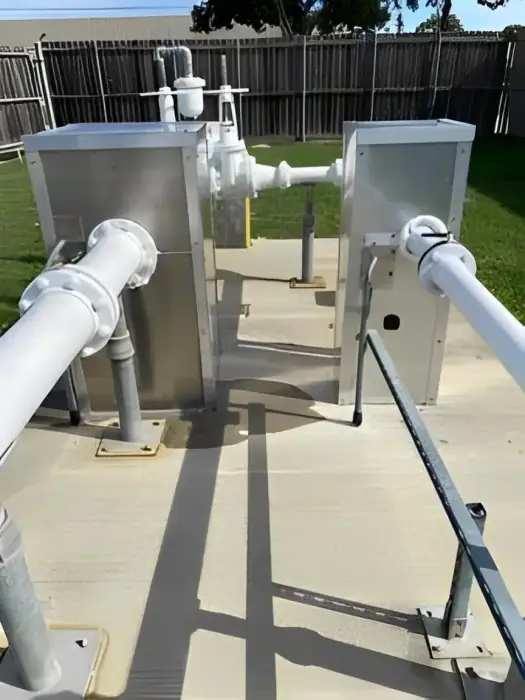 Two aluminum backflow enclosures and white piping on a concrete pad