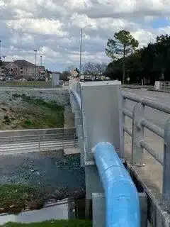Blue water main and aluminum enclosure along a roadside bridge