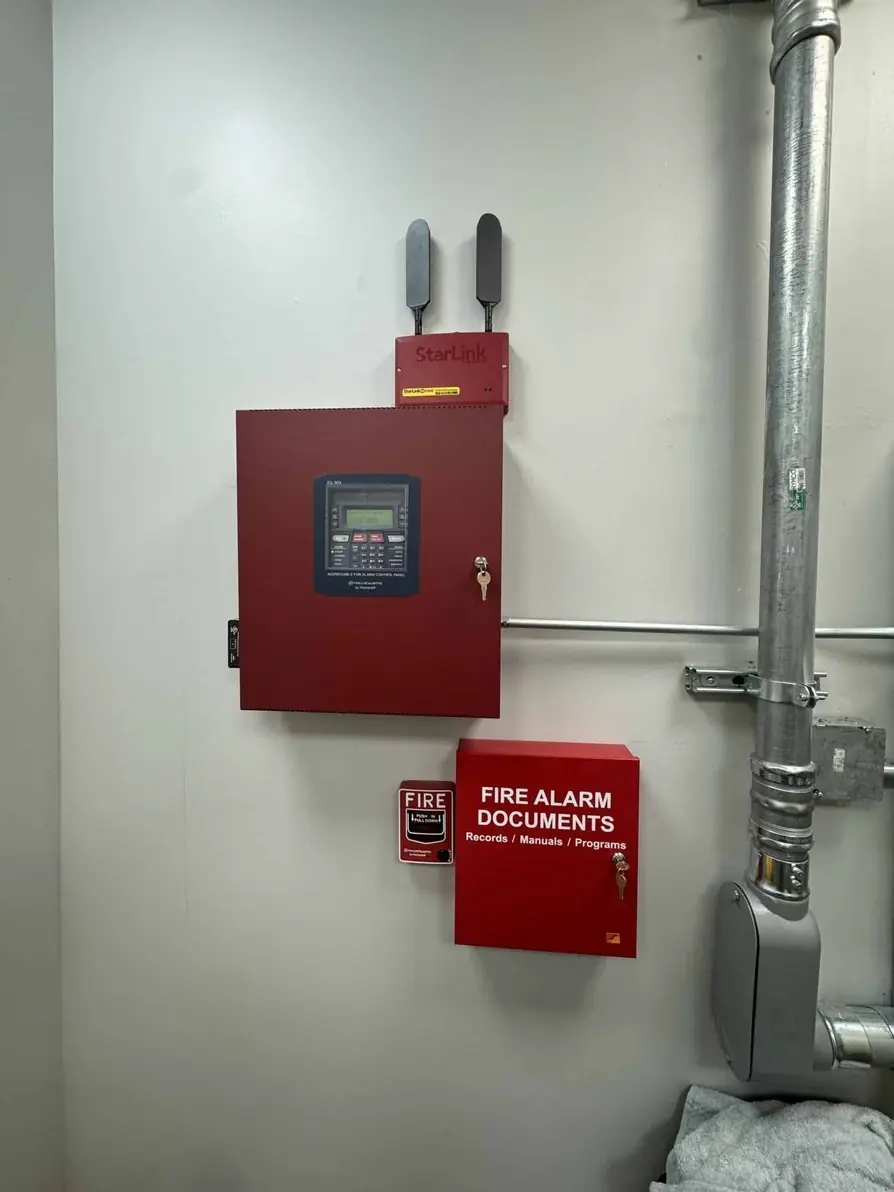 Commercial fire alarm control panel and documents box beside a steel pipe