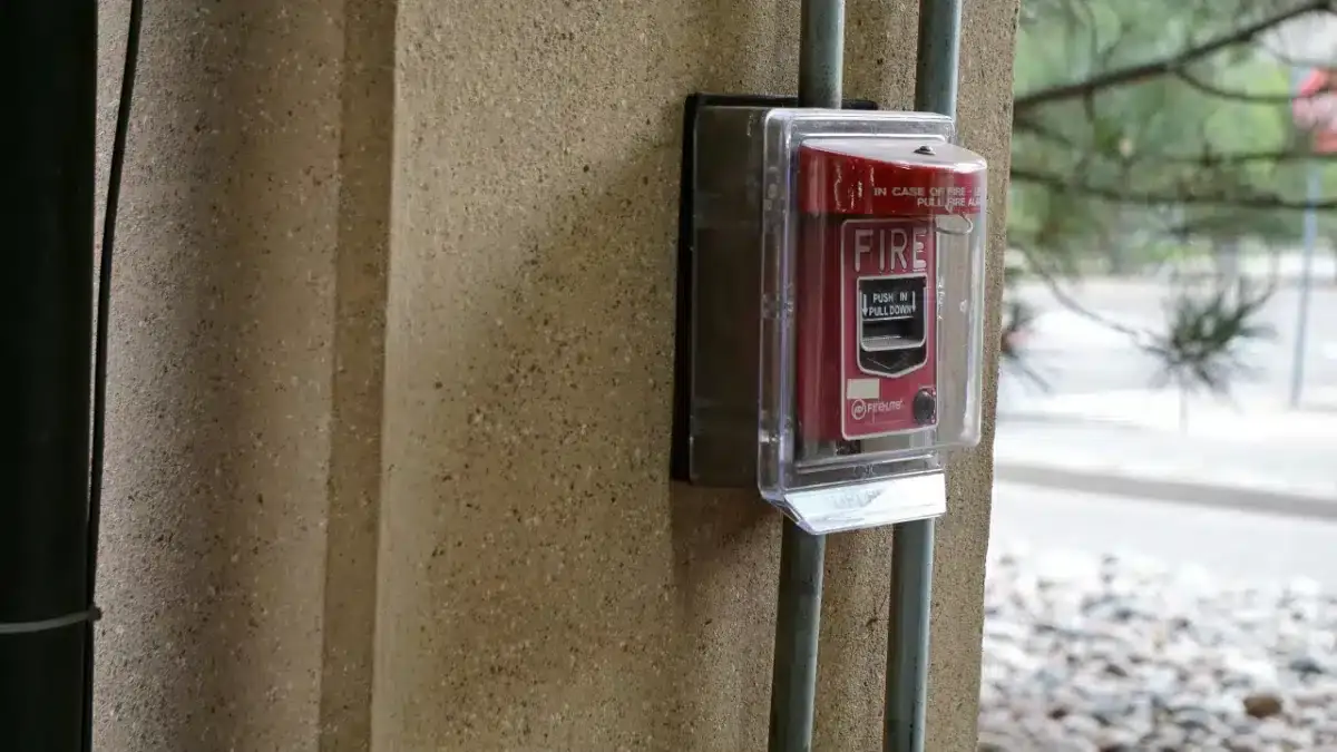 Red fire alarm pull station in a clear protective cover on an outdoor pillar