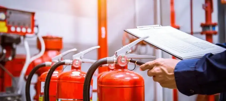 Technician with a clipboard inspecting a row of red fire extinguishers