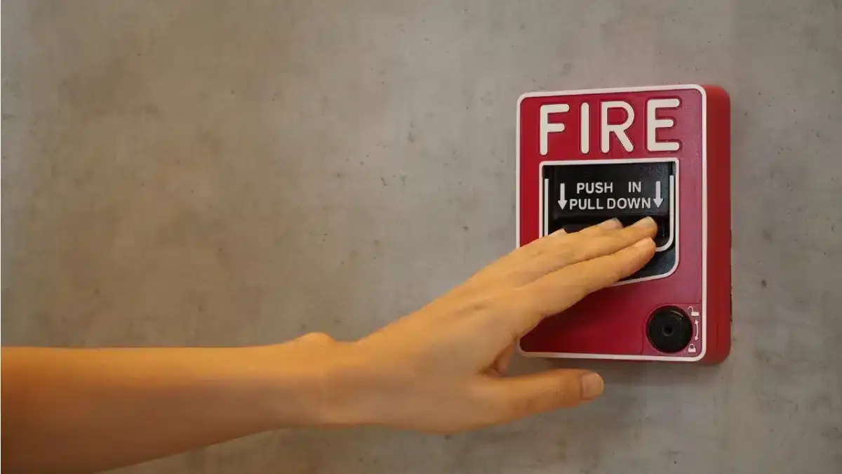 Hand pulling down a red fire alarm pull station on a concrete wall
