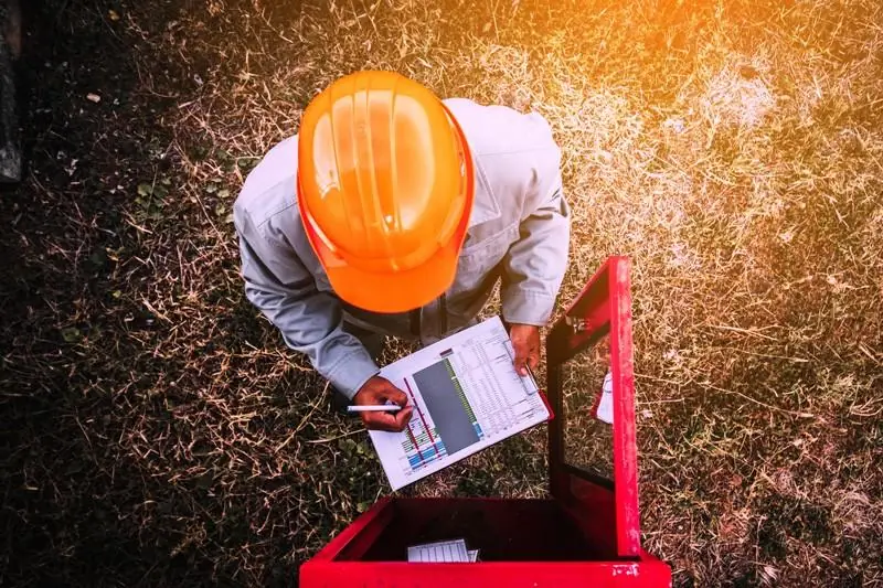 Inspector in an orange hard hat filling out a checklist over an open red box